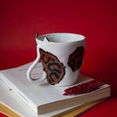 Handmade ceramic mug with a cat face design, available in calico, tuxedo, white, and orange cat variations. Perfect for cat lovers looking to add a cute, personalized touch to their drinkware collection.