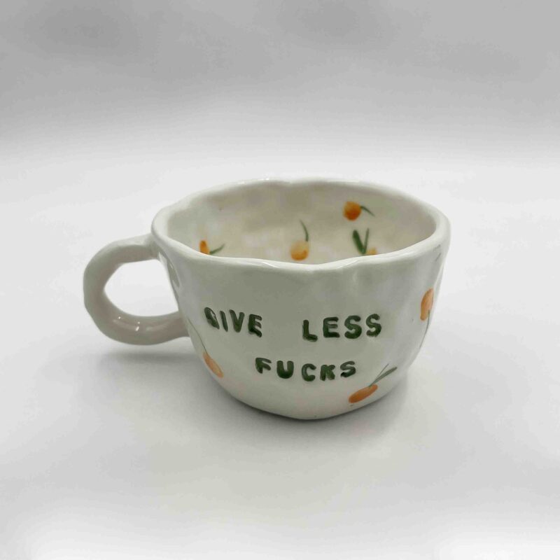 Handmade ceramic mugs adorned with playful fruit designs and the bold message 'Give Less Fucks' on the front. Perfect for adding a touch of humor and personality to your daily coffee or tea!" Greek: "Χειροποίητες κεραμικές κούπες διακοσμημένες με παιχνιδιάρικα σχέδια φρούτων και το τολμηρό μήνυμα 'Give Less Fucks' μπροστά. Ιδανικές για να προσθέσετε χιούμορ και προσωπικότητα στον καθημερινό σας καφέ ή τσάι!