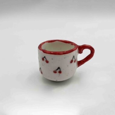 Handmade single espresso cup adorned with a charming cherry design. A delightful choice for coffee lovers who enjoy a touch of sweetness in their style. Χειροποίητο φλιτζάνι εσπρέσο διακοσμημένο με ένα χαριτωμένο σχέδιο κερασιών. Μια απολαυστική επιλογή για τους λάτρεις του καφέ που εκτιμούν μια δόση γλυκύτητας στο στυλ τους.