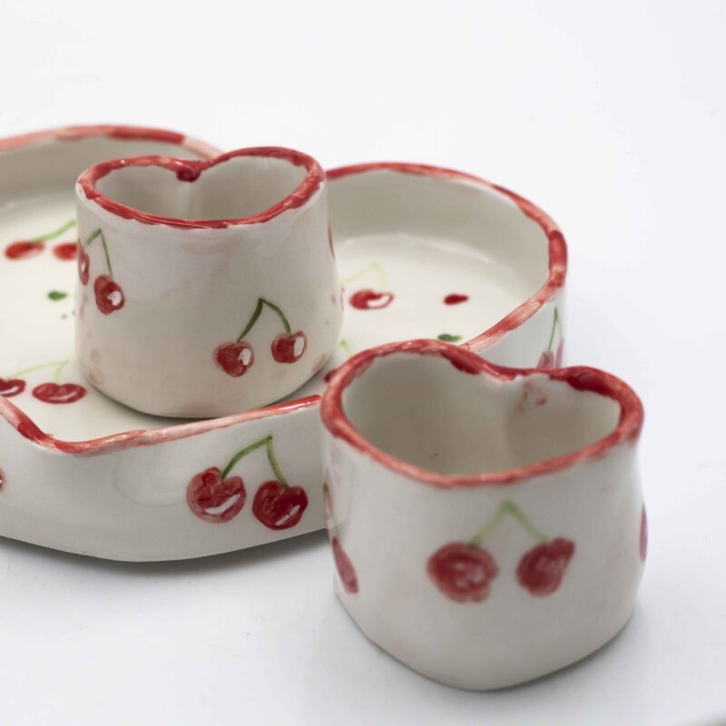 Handmade ceramic heart-shaped set, featuring a large heart plate and two matching heart cups, beautifully hand-painted with cherries. A romantic and charming design, perfect for sharing special moments over coffee or tea. Ideal for Valentine's Day, anniversaries, or as a unique gift for someone you love." Χειροποίητο κεραμικό σετ σε σχήμα καρδιάς, που περιλαμβάνει ένα μεγάλο πιάτο καρδιά και δύο ασορτί κούπες, διακοσμημένα με ζωγραφισμένα στο χέρι κεράσια. Ένα ρομαντικό και γοητευτικό σχέδιο, ιδανικό για να μοιράζεστε ξεχωριστές στιγμές με καφέ ή τσάι. Τέλειο για την Ημέρα του Αγίου Βαλεντίνου, επετείους ή ως μοναδικό δώρο για ένα αγαπημένο σας πρόσωπο.