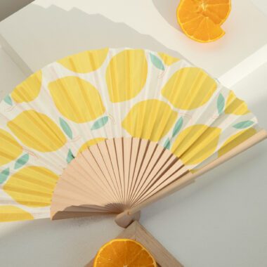 Feel the refreshing vibes of summer with the Citrus Breeze folding fan by Helio Ferretti. Decorated with vibrant citrus fruit patterns, this lightweight and portable fan keeps you cool on hot days while adding a stylish accent to your outfit. Perfect for outdoor events, travel, or everyday use.Νιώσε τη δροσιά του καλοκαιριού με τη βεντάλια Citrus Breeze από την Helio Ferretti. Διακοσμημένη με ζωηρά μοτίβα εσπεριδοειδών, αυτή η ελαφριά και φορητή βεντάλια σε κρατάει δροσερό στις ζεστές μέρες, προσθέτοντας ταυτόχρονα στυλ στην εμφάνισή σου. Ιδανική για εξωτερικές δραστηριότητες, ταξίδια ή καθημερινή χρήση.