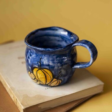 Handmade ceramic blue mug with pumpkins. shaped like a cauldron. For Halloween and fall vibes all the way.