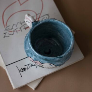 Handmade ceramic mug with a cloud-shaped handle and painted cloud faces featuring shiny eyes in an angelic core aesthetic. Soft blue and pink tones create a dreamy, sweet atmosphere. Each mug is one of a kind — hand-shaped and hand-painted, a small personal piece of art for those who love unique creations. Χειροποίητη κεραμική κούπα με χερούλι σε σχήμα συννεφιού και ζωγραφιστά συννεφάκια με εκφραστικά προσωπάκια και γυαλιστερά μάτια σε angelic core αισθητική. Οι απαλοί τόνοι του γαλάζιου και του ροζ προσδίδουν μια ονειρική, γλυκιά αίσθηση. Κάθε κούπα είναι μοναδική, πλασμένη και ζωγραφισμένη στο χέρι, ένα μικρό προσωπικό έργο τέχνης για κάθε λάτρη των ιδιαίτερων αντικειμένων.