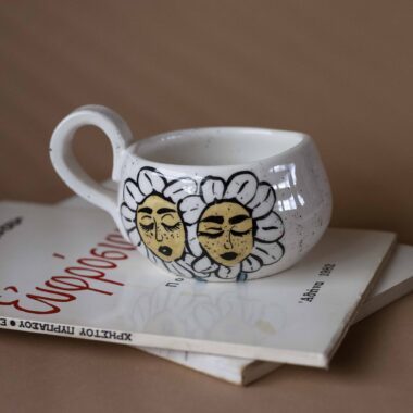 Χειροποίητη κεραμική κούπα διακοσμημένη με ζωγραφιστές μαργαρίτες και πολύχρωμα λουλούδια, όλα με γλυκά προσωπάκια και εκφραστικά μάτια. Πλασμένη και ζωγραφισμένη στο χέρι, κάθε κούπα είναι ένα μοναδικό έργο τέχνης που συνδυάζει τη φρεσκάδα της φύσης με μια παιχνιδιάρικη, ονειρική αισθητική. Ιδανική για όσους αγαπούν τα λουλούδια και τη χειροποίητη δημιουργία. Handmade ceramic mug decorated with painted daisies and colorful flowers, each featuring cute little faces with expressive eyes. Hand-shaped and hand-painted, every mug is a one-of-a-kind piece of art that blends the freshness of nature with a playful, dreamy aesthetic. Perfect for flower lovers and fans of handmade craftsmanship.