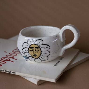 Χειροποίητη κεραμική κούπα διακοσμημένη με ζωγραφιστές μαργαρίτες και πολύχρωμα λουλούδια, όλα με γλυκά προσωπάκια και εκφραστικά μάτια. Πλασμένη και ζωγραφισμένη στο χέρι, κάθε κούπα είναι ένα μοναδικό έργο τέχνης που συνδυάζει τη φρεσκάδα της φύσης με μια παιχνιδιάρικη, ονειρική αισθητική. Ιδανική για όσους αγαπούν τα λουλούδια και τη χειροποίητη δημιουργία. Handmade ceramic mug decorated with painted daisies and colorful flowers, each featuring cute little faces with expressive eyes. Hand-shaped and hand-painted, every mug is a one-of-a-kind piece of art that blends the freshness of nature with a playful, dreamy aesthetic. Perfect for flower lovers and fans of handmade craftsmanship.