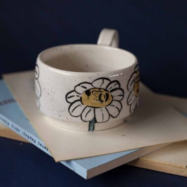 Χειροποίητη κεραμική κούπα διακοσμημένη με ζωγραφιστές μαργαρίτες και πολύχρωμα λουλούδια, όλα με γλυκά προσωπάκια και εκφραστικά μάτια. Πλασμένη και ζωγραφισμένη στο χέρι, κάθε κούπα είναι ένα μοναδικό έργο τέχνης που συνδυάζει τη φρεσκάδα της φύσης με μια παιχνιδιάρικη, ονειρική αισθητική. Ιδανική για όσους αγαπούν τα λουλούδια και τη χειροποίητη δημιουργία. Handmade ceramic mug decorated with painted daisies and colorful flowers, each featuring cute little faces with expressive eyes. Hand-shaped and hand-painted, every mug is a one-of-a-kind piece of art that blends the freshness of nature with a playful, dreamy aesthetic. Perfect for flower lovers and fans of handmade craftsmanship.