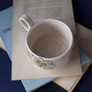 Χειροποίητη κεραμική κούπα διακοσμημένη με ζωγραφιστές μαργαρίτες και πολύχρωμα λουλούδια, όλα με γλυκά προσωπάκια και εκφραστικά μάτια. Πλασμένη και ζωγραφισμένη στο χέρι, κάθε κούπα είναι ένα μοναδικό έργο τέχνης που συνδυάζει τη φρεσκάδα της φύσης με μια παιχνιδιάρικη, ονειρική αισθητική. Ιδανική για όσους αγαπούν τα λουλούδια και τη χειροποίητη δημιουργία. Handmade ceramic mug decorated with painted daisies and colorful flowers, each featuring cute little faces with expressive eyes. Hand-shaped and hand-painted, every mug is a one-of-a-kind piece of art that blends the freshness of nature with a playful, dreamy aesthetic. Perfect for flower lovers and fans of handmade craftsmanship.