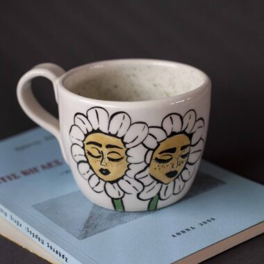 Χειροποίητη κεραμική κούπα διακοσμημένη με ζωγραφιστές μαργαρίτες και πολύχρωμα λουλούδια, όλα με γλυκά προσωπάκια και εκφραστικά μάτια. Πλασμένη και ζωγραφισμένη στο χέρι, κάθε κούπα είναι ένα μοναδικό έργο τέχνης που συνδυάζει τη φρεσκάδα της φύσης με μια παιχνιδιάρικη, ονειρική αισθητική. Ιδανική για όσους αγαπούν τα λουλούδια και τη χειροποίητη δημιουργία. Handmade ceramic mug decorated with painted daisies and colorful flowers, each featuring cute little faces with expressive eyes. Hand-shaped and hand-painted, every mug is a one-of-a-kind piece of art that blends the freshness of nature with a playful, dreamy aesthetic. Perfect for flower lovers and fans of handmade craftsmanship.