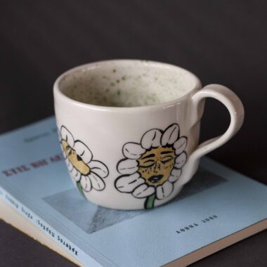 Χειροποίητη κεραμική κούπα διακοσμημένη με ζωγραφιστές μαργαρίτες και πολύχρωμα λουλούδια, όλα με γλυκά προσωπάκια και εκφραστικά μάτια. Πλασμένη και ζωγραφισμένη στο χέρι, κάθε κούπα είναι ένα μοναδικό έργο τέχνης που συνδυάζει τη φρεσκάδα της φύσης με μια παιχνιδιάρικη, ονειρική αισθητική. Ιδανική για όσους αγαπούν τα λουλούδια και τη χειροποίητη δημιουργία. Handmade ceramic mug decorated with painted daisies and colorful flowers, each featuring cute little faces with expressive eyes. Hand-shaped and hand-painted, every mug is a one-of-a-kind piece of art that blends the freshness of nature with a playful, dreamy aesthetic. Perfect for flower lovers and fans of handmade craftsmanship.