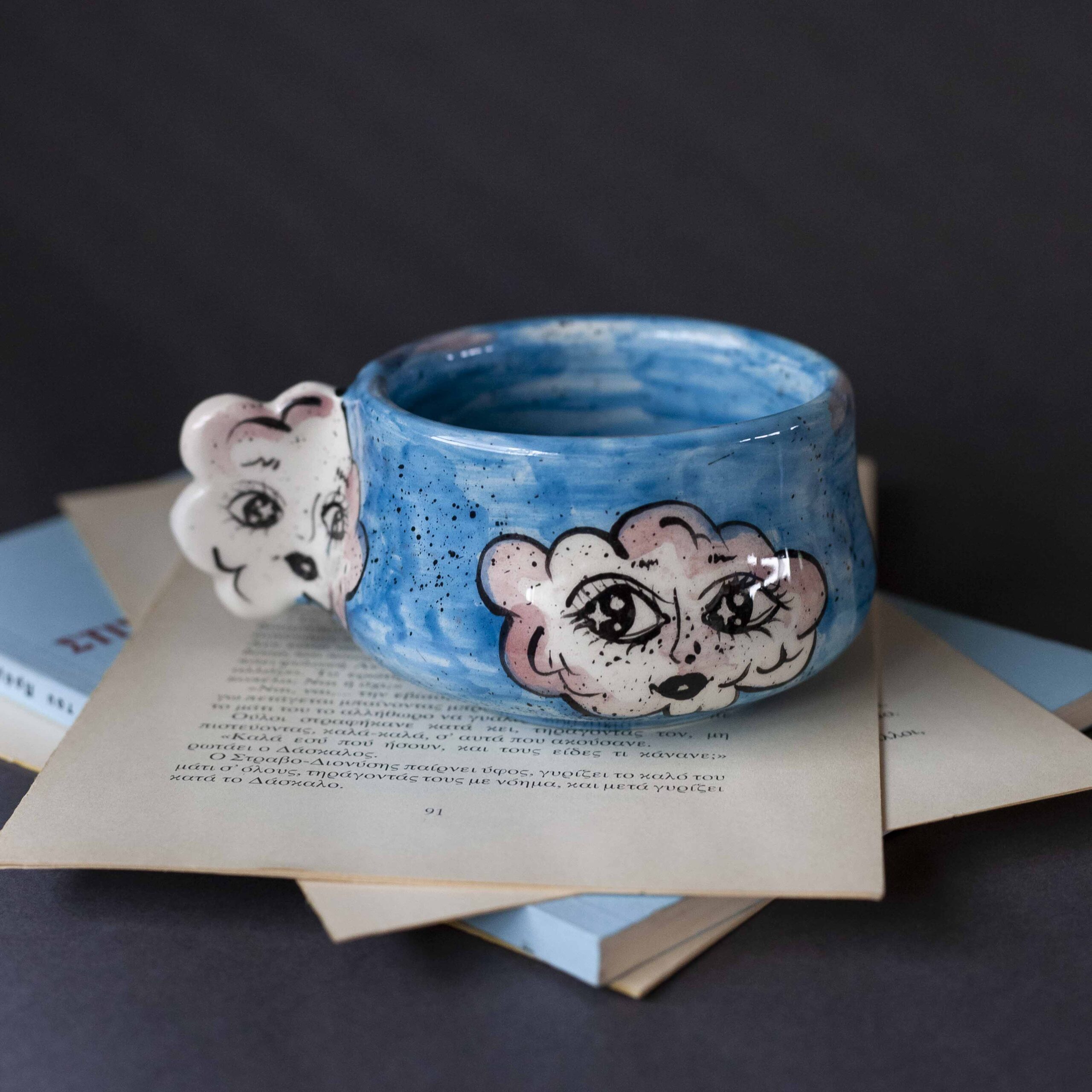 Handmade ceramic mug with a cloud-shaped handle and painted cloud faces featuring shiny eyes in an angelic core aesthetic. Soft blue and pink tones create a dreamy, sweet atmosphere. Each mug is one of a kind — hand-shaped and hand-painted, a small personal piece of art for those who love unique creations. Χειροποίητη κεραμική κούπα με χερούλι σε σχήμα συννεφιού και ζωγραφιστά συννεφάκια με εκφραστικά προσωπάκια και γυαλιστερά μάτια σε angelic core αισθητική. Οι απαλοί τόνοι του γαλάζιου και του ροζ προσδίδουν μια ονειρική, γλυκιά αίσθηση. Κάθε κούπα είναι μοναδική, πλασμένη και ζωγραφισμένη στο χέρι, ένα μικρό προσωπικό έργο τέχνης για κάθε λάτρη των ιδιαίτερων αντικειμένων.