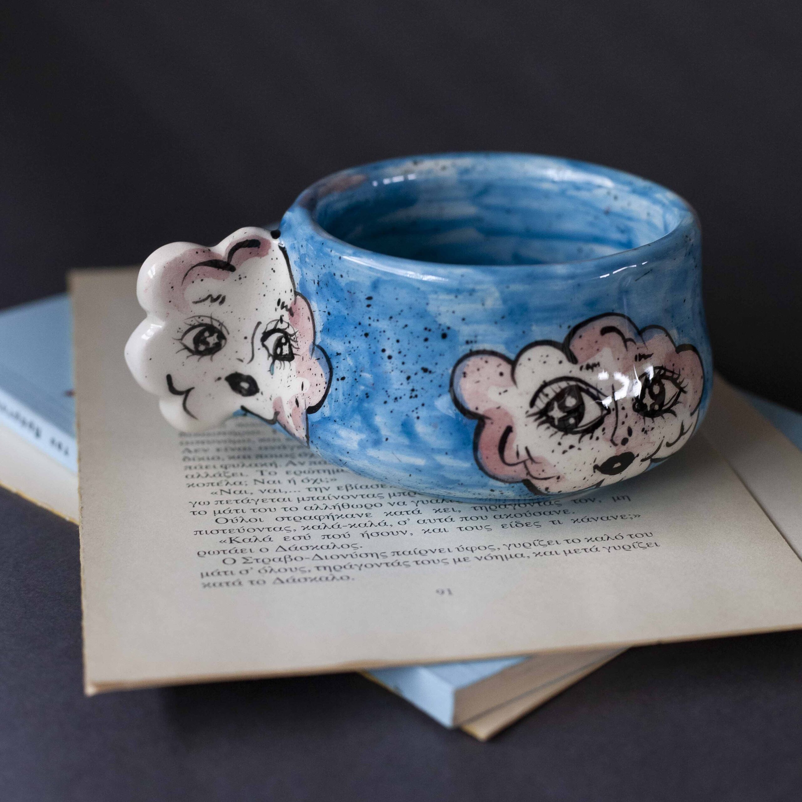 Handmade ceramic mug with a cloud-shaped handle and painted cloud faces featuring shiny eyes in an angelic core aesthetic. Soft blue and pink tones create a dreamy, sweet atmosphere. Each mug is one of a kind — hand-shaped and hand-painted, a small personal piece of art for those who love unique creations. Χειροποίητη κεραμική κούπα με χερούλι σε σχήμα συννεφιού και ζωγραφιστά συννεφάκια με εκφραστικά προσωπάκια και γυαλιστερά μάτια σε angelic core αισθητική. Οι απαλοί τόνοι του γαλάζιου και του ροζ προσδίδουν μια ονειρική, γλυκιά αίσθηση. Κάθε κούπα είναι μοναδική, πλασμένη και ζωγραφισμένη στο χέρι, ένα μικρό προσωπικό έργο τέχνης για κάθε λάτρη των ιδιαίτερων αντικειμένων.