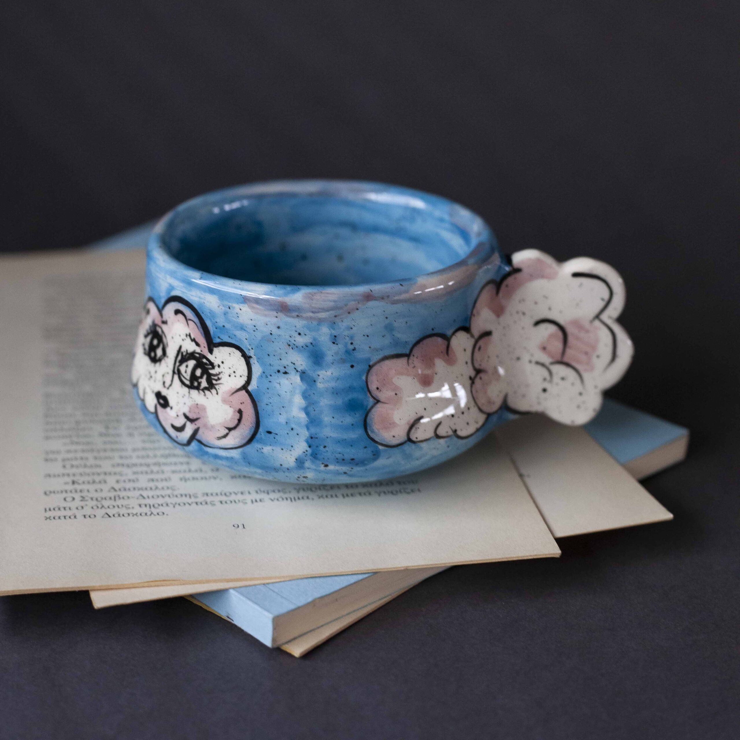 Handmade ceramic mug with a cloud-shaped handle and painted cloud faces featuring shiny eyes in an angelic core aesthetic. Soft blue and pink tones create a dreamy, sweet atmosphere. Each mug is one of a kind — hand-shaped and hand-painted, a small personal piece of art for those who love unique creations. Χειροποίητη κεραμική κούπα με χερούλι σε σχήμα συννεφιού και ζωγραφιστά συννεφάκια με εκφραστικά προσωπάκια και γυαλιστερά μάτια σε angelic core αισθητική. Οι απαλοί τόνοι του γαλάζιου και του ροζ προσδίδουν μια ονειρική, γλυκιά αίσθηση. Κάθε κούπα είναι μοναδική, πλασμένη και ζωγραφισμένη στο χέρι, ένα μικρό προσωπικό έργο τέχνης για κάθε λάτρη των ιδιαίτερων αντικειμένων.