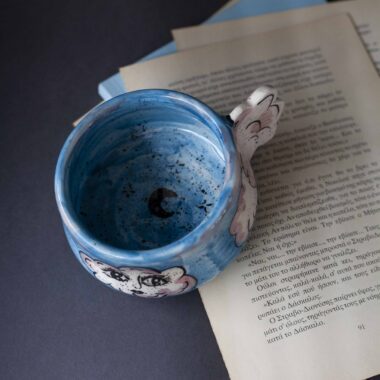 Handmade ceramic mug with a cloud-shaped handle and painted cloud faces featuring shiny eyes in an angelic core aesthetic. Soft blue and pink tones create a dreamy, sweet atmosphere. Each mug is one of a kind — hand-shaped and hand-painted, a small personal piece of art for those who love unique creations. Χειροποίητη κεραμική κούπα με χερούλι σε σχήμα συννεφιού και ζωγραφιστά συννεφάκια με εκφραστικά προσωπάκια και γυαλιστερά μάτια σε angelic core αισθητική. Οι απαλοί τόνοι του γαλάζιου και του ροζ προσδίδουν μια ονειρική, γλυκιά αίσθηση. Κάθε κούπα είναι μοναδική, πλασμένη και ζωγραφισμένη στο χέρι, ένα μικρό προσωπικό έργο τέχνης για κάθε λάτρη των ιδιαίτερων αντικειμένων.