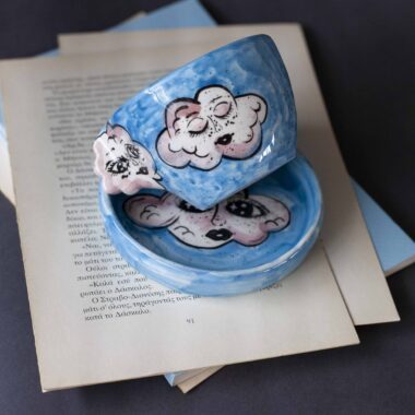 Handmade ceramic mug with a cloud-shaped handle and painted cloud faces featuring shiny eyes in an angelic core aesthetic. Soft blue and pink tones create a dreamy, sweet atmosphere. Each mug is one of a kind — hand-shaped and hand-painted, a small personal piece of art for those who love unique creations. Χειροποίητη κεραμική κούπα με χερούλι σε σχήμα συννεφιού και ζωγραφιστά συννεφάκια με εκφραστικά προσωπάκια και γυαλιστερά μάτια σε angelic core αισθητική. Οι απαλοί τόνοι του γαλάζιου και του ροζ προσδίδουν μια ονειρική, γλυκιά αίσθηση. Κάθε κούπα είναι μοναδική, πλασμένη και ζωγραφισμένη στο χέρι, ένα μικρό προσωπικό έργο τέχνης για κάθε λάτρη των ιδιαίτερων αντικειμένων.