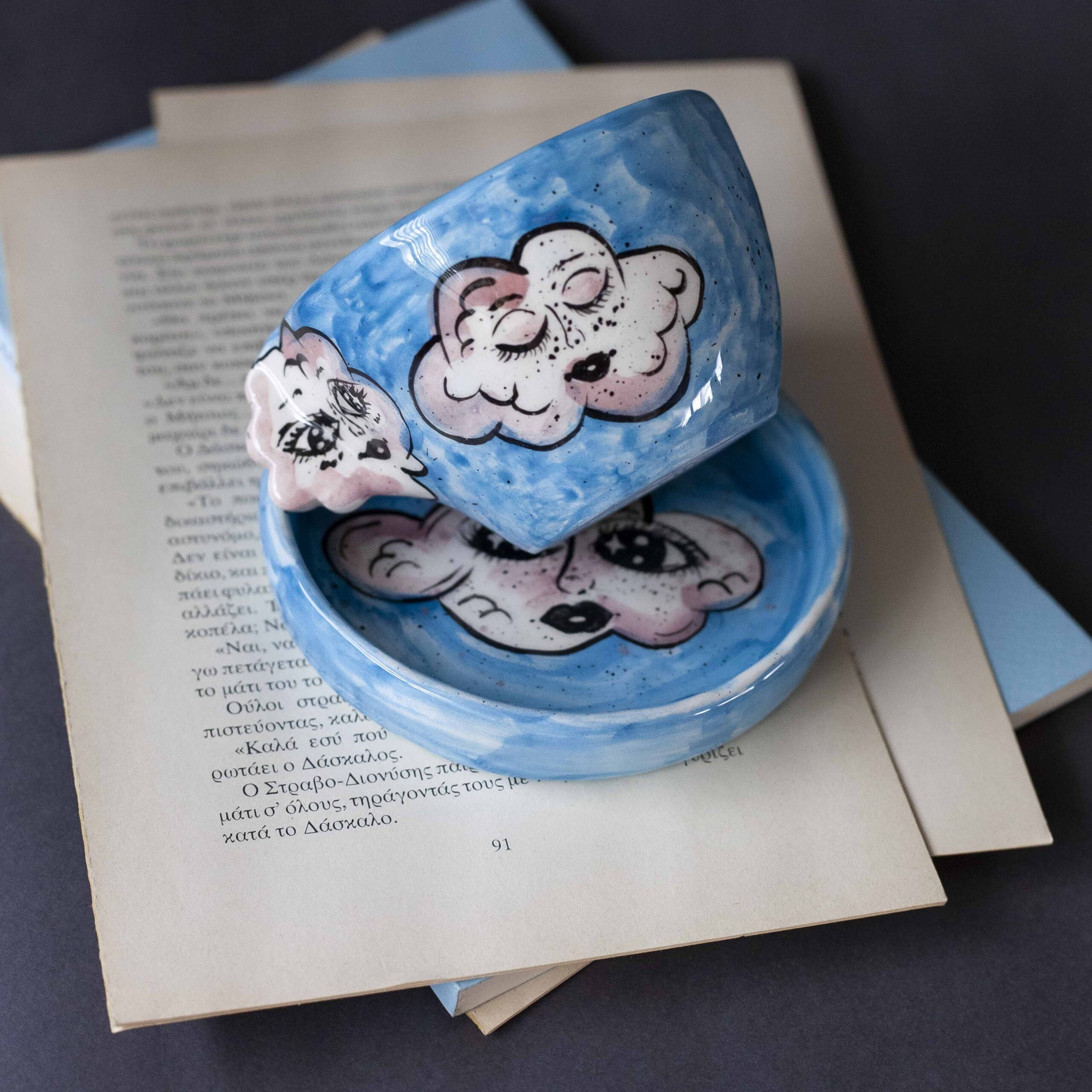 Handmade ceramic mug with a cloud-shaped handle and painted cloud faces featuring shiny eyes in an angelic core aesthetic. Soft blue and pink tones create a dreamy, sweet atmosphere. Each mug is one of a kind — hand-shaped and hand-painted, a small personal piece of art for those who love unique creations. Χειροποίητη κεραμική κούπα με χερούλι σε σχήμα συννεφιού και ζωγραφιστά συννεφάκια με εκφραστικά προσωπάκια και γυαλιστερά μάτια σε angelic core αισθητική. Οι απαλοί τόνοι του γαλάζιου και του ροζ προσδίδουν μια ονειρική, γλυκιά αίσθηση. Κάθε κούπα είναι μοναδική, πλασμένη και ζωγραφισμένη στο χέρι, ένα μικρό προσωπικό έργο τέχνης για κάθε λάτρη των ιδιαίτερων αντικειμένων.
