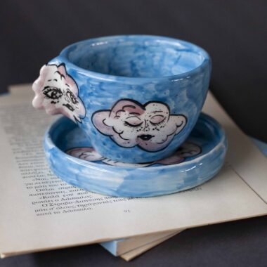 Handmade ceramic mug with a cloud-shaped handle and painted cloud faces featuring shiny eyes in an angelic core aesthetic. Soft blue and pink tones create a dreamy, sweet atmosphere. Each mug is one of a kind — hand-shaped and hand-painted, a small personal piece of art for those who love unique creations. Χειροποίητη κεραμική κούπα με χερούλι σε σχήμα συννεφιού και ζωγραφιστά συννεφάκια με εκφραστικά προσωπάκια και γυαλιστερά μάτια σε angelic core αισθητική. Οι απαλοί τόνοι του γαλάζιου και του ροζ προσδίδουν μια ονειρική, γλυκιά αίσθηση. Κάθε κούπα είναι μοναδική, πλασμένη και ζωγραφισμένη στο χέρι, ένα μικρό προσωπικό έργο τέχνης για κάθε λάτρη των ιδιαίτερων αντικειμένων.