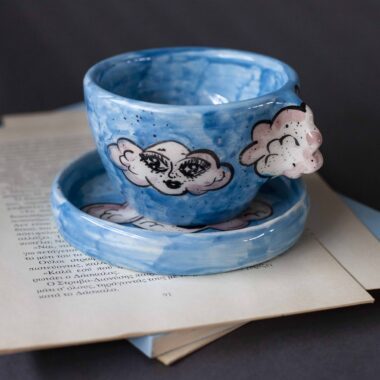 Handmade ceramic mug with a cloud-shaped handle and painted cloud faces featuring shiny eyes in an angelic core aesthetic. Soft blue and pink tones create a dreamy, sweet atmosphere. Each mug is one of a kind — hand-shaped and hand-painted, a small personal piece of art for those who love unique creations. Χειροποίητη κεραμική κούπα με χερούλι σε σχήμα συννεφιού και ζωγραφιστά συννεφάκια με εκφραστικά προσωπάκια και γυαλιστερά μάτια σε angelic core αισθητική. Οι απαλοί τόνοι του γαλάζιου και του ροζ προσδίδουν μια ονειρική, γλυκιά αίσθηση. Κάθε κούπα είναι μοναδική, πλασμένη και ζωγραφισμένη στο χέρι, ένα μικρό προσωπικό έργο τέχνης για κάθε λάτρη των ιδιαίτερων αντικειμένων.
