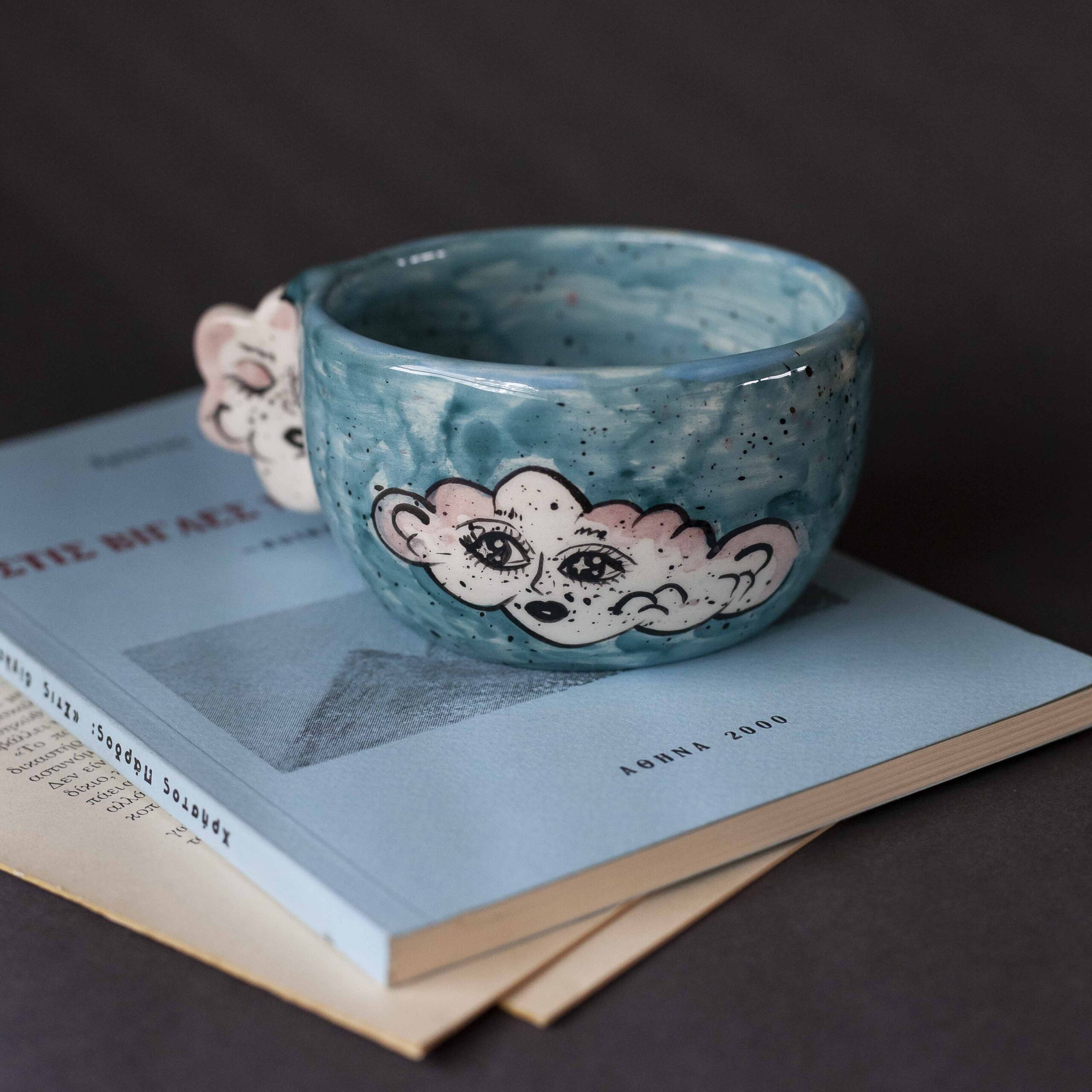 Handmade ceramic mug with a cloud-shaped handle and painted cloud faces featuring shiny eyes in an angelic core aesthetic. Soft blue and pink tones create a dreamy, sweet atmosphere. Each mug is one of a kind — hand-shaped and hand-painted, a small personal piece of art for those who love unique creations. Χειροποίητη κεραμική κούπα με χερούλι σε σχήμα συννεφιού και ζωγραφιστά συννεφάκια με εκφραστικά προσωπάκια και γυαλιστερά μάτια σε angelic core αισθητική. Οι απαλοί τόνοι του γαλάζιου και του ροζ προσδίδουν μια ονειρική, γλυκιά αίσθηση. Κάθε κούπα είναι μοναδική, πλασμένη και ζωγραφισμένη στο χέρι, ένα μικρό προσωπικό έργο τέχνης για κάθε λάτρη των ιδιαίτερων αντικειμένων.