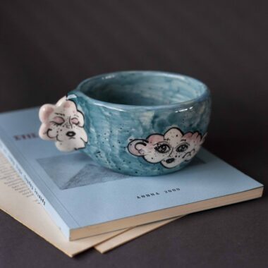 Handmade ceramic mug with a cloud-shaped handle and painted cloud faces featuring shiny eyes in an angelic core aesthetic. Soft blue and pink tones create a dreamy, sweet atmosphere. Each mug is one of a kind — hand-shaped and hand-painted, a small personal piece of art for those who love unique creations. Χειροποίητη κεραμική κούπα με χερούλι σε σχήμα συννεφιού και ζωγραφιστά συννεφάκια με εκφραστικά προσωπάκια και γυαλιστερά μάτια σε angelic core αισθητική. Οι απαλοί τόνοι του γαλάζιου και του ροζ προσδίδουν μια ονειρική, γλυκιά αίσθηση. Κάθε κούπα είναι μοναδική, πλασμένη και ζωγραφισμένη στο χέρι, ένα μικρό προσωπικό έργο τέχνης για κάθε λάτρη των ιδιαίτερων αντικειμένων.
