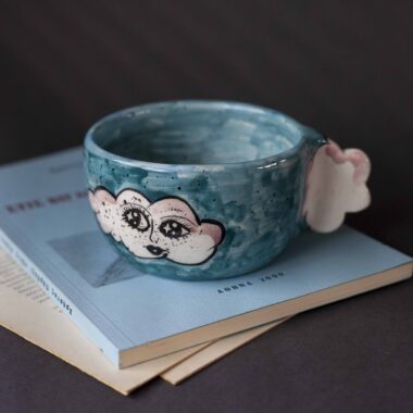 Handmade ceramic mug with a cloud-shaped handle and painted cloud faces featuring shiny eyes in an angelic core aesthetic. Soft blue and pink tones create a dreamy, sweet atmosphere. Each mug is one of a kind — hand-shaped and hand-painted, a small personal piece of art for those who love unique creations. Χειροποίητη κεραμική κούπα με χερούλι σε σχήμα συννεφιού και ζωγραφιστά συννεφάκια με εκφραστικά προσωπάκια και γυαλιστερά μάτια σε angelic core αισθητική. Οι απαλοί τόνοι του γαλάζιου και του ροζ προσδίδουν μια ονειρική, γλυκιά αίσθηση. Κάθε κούπα είναι μοναδική, πλασμένη και ζωγραφισμένη στο χέρι, ένα μικρό προσωπικό έργο τέχνης για κάθε λάτρη των ιδιαίτερων αντικειμένων.