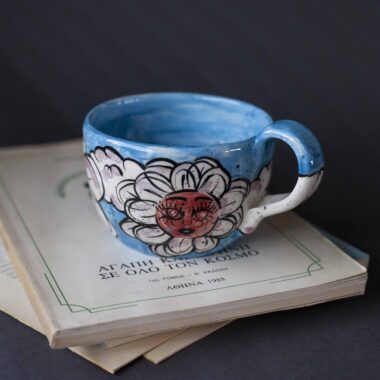 Χειροποίητη κεραμική κούπα διακοσμημένη με ζωγραφιστές μαργαρίτες και πολύχρωμα λουλούδια, όλα με γλυκά προσωπάκια και εκφραστικά μάτια. Πλασμένη και ζωγραφισμένη στο χέρι, κάθε κούπα είναι ένα μοναδικό έργο τέχνης που συνδυάζει τη φρεσκάδα της φύσης με μια παιχνιδιάρικη, ονειρική αισθητική. Ιδανική για όσους αγαπούν τα λουλούδια και τη χειροποίητη δημιουργία. Handmade ceramic mug decorated with painted daisies and colorful flowers, each featuring cute little faces with expressive eyes. Hand-shaped and hand-painted, every mug is a one-of-a-kind piece of art that blends the freshness of nature with a playful, dreamy aesthetic. Perfect for flower lovers and fans of handmade craftsmanship.