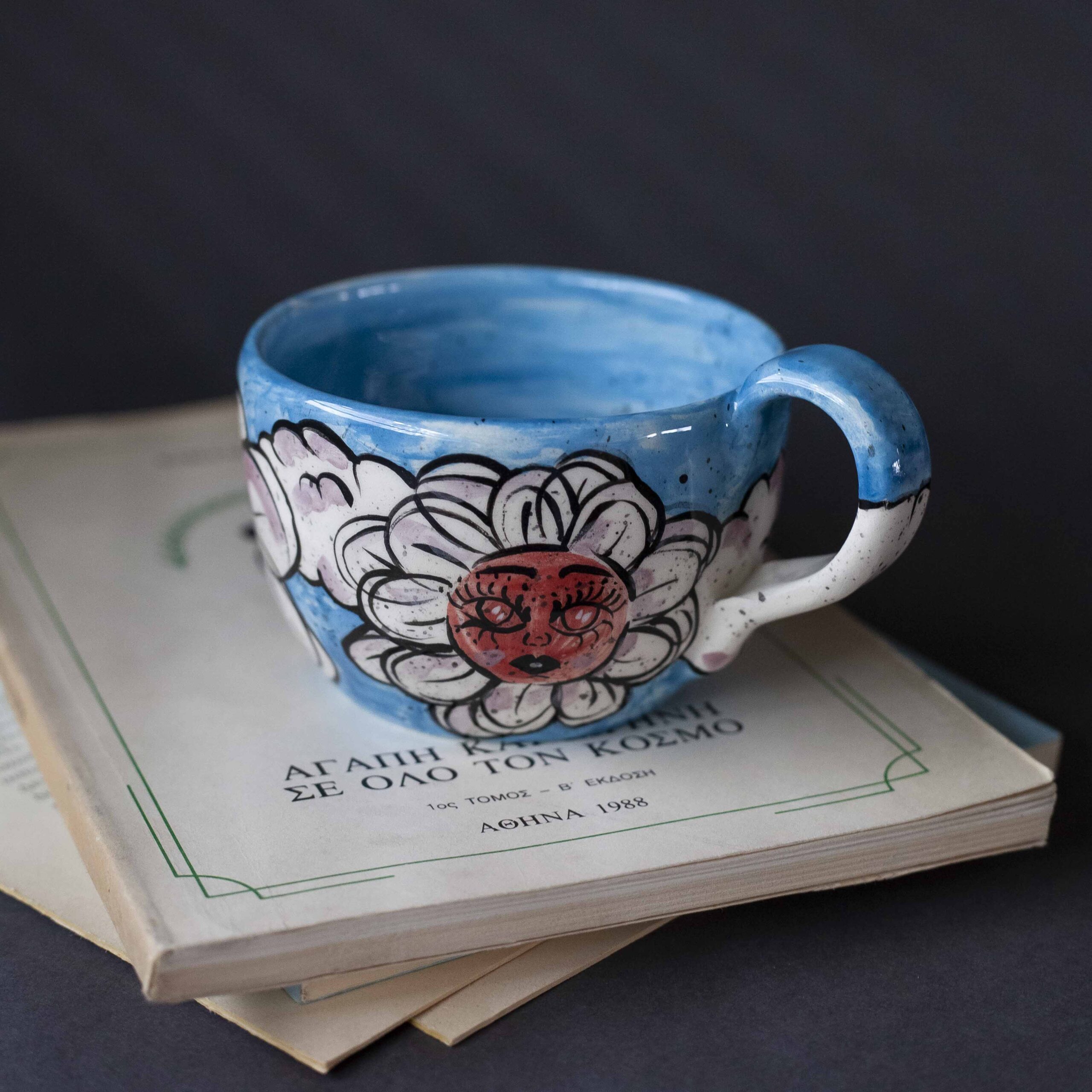 Χειροποίητη κεραμική κούπα διακοσμημένη με ζωγραφιστές μαργαρίτες και πολύχρωμα λουλούδια, όλα με γλυκά προσωπάκια και εκφραστικά μάτια. Πλασμένη και ζωγραφισμένη στο χέρι, κάθε κούπα είναι ένα μοναδικό έργο τέχνης που συνδυάζει τη φρεσκάδα της φύσης με μια παιχνιδιάρικη, ονειρική αισθητική. Ιδανική για όσους αγαπούν τα λουλούδια και τη χειροποίητη δημιουργία. Handmade ceramic mug decorated with painted daisies and colorful flowers, each featuring cute little faces with expressive eyes. Hand-shaped and hand-painted, every mug is a one-of-a-kind piece of art that blends the freshness of nature with a playful, dreamy aesthetic. Perfect for flower lovers and fans of handmade craftsmanship.