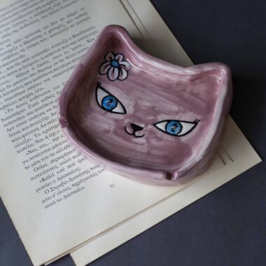 Χειροποίητα κεραμικά τασάκια και κούπες με σχέδια γατών, κάθε μία με ξεχωριστή έκφραση και χαρακτήρα. Πλασμένες και ζωγραφισμένες στο χέρι με ζωηρά χρώματα και καλλιτεχνικές λεπτομέρειες, ιδανικές για τους λάτρεις των γατών και της χειροποίητης τέχνης. Handmade ceramic cat-themed ashtrays and mugs, each featuring unique cat expressions and artistic charm. Hand-shaped and hand-painted with lively colors and creative details — perfect for cat lovers and fans of handmade artistry.