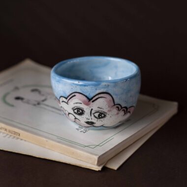 Handmade ceramic mug with a cloud-shaped handle and painted cloud faces featuring shiny eyes in an angelic core aesthetic. Soft blue and pink tones create a dreamy, sweet atmosphere. Each mug is one of a kind — hand-shaped and hand-painted, a small personal piece of art for those who love unique creations. Χειροποίητη κεραμική κούπα με χερούλι σε σχήμα συννεφιού και ζωγραφιστά συννεφάκια με εκφραστικά προσωπάκια και γυαλιστερά μάτια σε angelic core αισθητική. Οι απαλοί τόνοι του γαλάζιου και του ροζ προσδίδουν μια ονειρική, γλυκιά αίσθηση. Κάθε κούπα είναι μοναδική, πλασμένη και ζωγραφισμένη στο χέρι, ένα μικρό προσωπικό έργο τέχνης για κάθε λάτρη των ιδιαίτερων αντικειμένων.