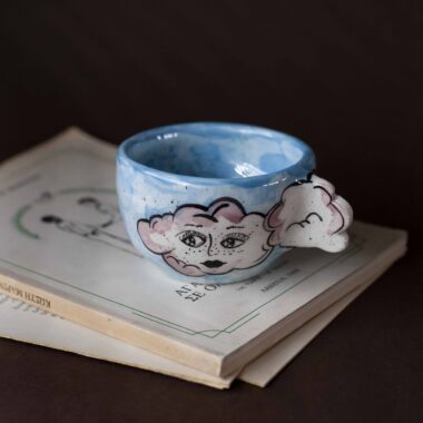 Handmade ceramic mug with a cloud-shaped handle and painted cloud faces featuring shiny eyes in an angelic core aesthetic. Soft blue and pink tones create a dreamy, sweet atmosphere. Each mug is one of a kind — hand-shaped and hand-painted, a small personal piece of art for those who love unique creations. Χειροποίητη κεραμική κούπα με χερούλι σε σχήμα συννεφιού και ζωγραφιστά συννεφάκια με εκφραστικά προσωπάκια και γυαλιστερά μάτια σε angelic core αισθητική. Οι απαλοί τόνοι του γαλάζιου και του ροζ προσδίδουν μια ονειρική, γλυκιά αίσθηση. Κάθε κούπα είναι μοναδική, πλασμένη και ζωγραφισμένη στο χέρι, ένα μικρό προσωπικό έργο τέχνης για κάθε λάτρη των ιδιαίτερων αντικειμένων.
