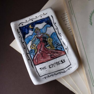 Χειροποίητα κεραμικά δισκάκια εμπνευσμένα από τα σύμβολα των καρτών ταρώ, ζωγραφισμένα στο χέρι με μυστικιστικά σχέδια και χρυσές λεπτομέρειες. Κάθε δίσκος είναι μοναδικός, ιδανικός για κοσμήματα, κρυστάλλους ή διακόσμηση με μαγική αισθητική. Handmade ceramic tarot-inspired trays, hand-painted with mystical symbols and golden details. Each piece is unique, perfect for holding jewelry, crystals, or simply adding a touch of magic to your decor.
