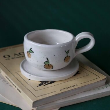 Χειροποίητα κεραμικά εσπρέσο κουπάκια με πιατάκι, διακοσμημένα με ζωγραφιστά φρουτάκια — πορτοκάλια, λεμόνια και αχλάδια — ανάμεσα σε μικρά λουλουδάκια. Οι δίχρωμοι συνδυασμοί και οι λεπτομέρειες στο χέρι χαρίζουν παιχνιδιάρικη και ζωντανή αισθητική. Κάθε σετ είναι μοναδικό, πλασμένο και ζωγραφισμένο στο χέρι, ιδανικό για να προσθέσει χρώμα και τέχνη σε κάθε στιγμή καφέ. Handmade ceramic espresso cup and saucer set, decorated with hand-painted fruits — oranges, lemons, and pears — surrounded by small flowers. The two-tone color combinations and fine hand-painted details give a lively, playful feel. Each set is one of a kind, crafted and painted by hand, perfect for adding a splash of color and artistry to your coffee moments.