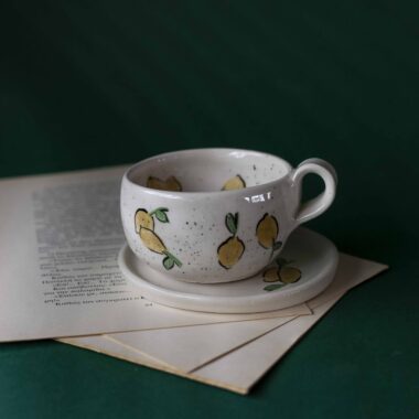 Χειροποίητα κεραμικά εσπρέσο κουπάκια με πιατάκι, διακοσμημένα με ζωγραφιστά φρουτάκια — πορτοκάλια, λεμόνια και αχλάδια — ανάμεσα σε μικρά λουλουδάκια. Οι δίχρωμοι συνδυασμοί και οι λεπτομέρειες στο χέρι χαρίζουν παιχνιδιάρικη και ζωντανή αισθητική. Κάθε σετ είναι μοναδικό, πλασμένο και ζωγραφισμένο στο χέρι, ιδανικό για να προσθέσει χρώμα και τέχνη σε κάθε στιγμή καφέ. Handmade ceramic espresso cup and saucer set, decorated with hand-painted fruits — oranges, lemons, and pears — surrounded by small flowers. The two-tone color combinations and fine hand-painted details give a lively, playful feel. Each set is one of a kind, crafted and painted by hand, perfect for adding a splash of color and artistry to your coffee moments.