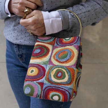 χειροποίητη χρωμάτιστή τσάντα σε μοτίβο του Wassily Kandinsky. Διάσημο έργο του με πολλά χρώματα. Γνωστό κυρίως για το παιχνίδι που κάνει το τετράγωνο με τους ασύμμετρους κύκλους. Το χερούλι της είναι ένας μεταλλικός κύκλος. handmade bag with a known pattern of wassily kandinsky. A famous art with multiple colors. It is known for the squares and the uneven circles in the middle. The handle of the bag is a metalic circle.