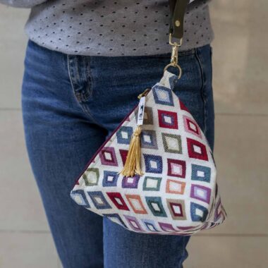 χειροποίητη τριγωνική τσαντούλα με δερμάτινο λουρί και κρεμαστή φούντα. Το μοτίβο της είναι πολύχρωμοι ρόμβοι. handmade triangle bag with leather handle and tassels. the pattern is colorful rhombus.