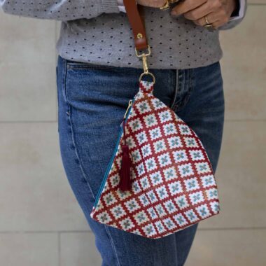 χειροποίητη τριγωνική τσαντούλα με δερμάτινο λουρί και κρεμαστή φούντα. Το μοτίβο της είναι καρό με τιρκουάζ σταυρούς. σε κόκκινες αποχρώσεις. handmade triangle bag with leather handle and tassels. the checkered pattern is red and it has small turquoise crosses .