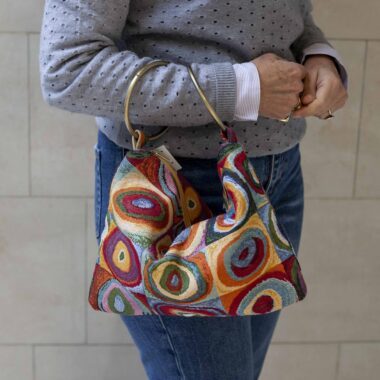 χειροποίητη χρωμάτιστή τσάντα σε μοτίβο του Wassily Kandinsky. Διάσημο έργο του με πολλά χρώματα. Γνωστό κυρίως για το παιχνίδι που κάνει το τετράγωνο με τους ασύμμετρους κύκλους. Το χερούλι της είναι δύο μεταλλικοί κρίκοι. handmade bag with a known pattern of wassily kandinsky. A famous art with multiple colors. It is known for the squares and the uneven circles in the middle. The handle of the bag is two metalic hoops.