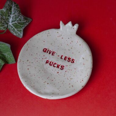 handmade plate with the quote give less fucks on it. with high temperature clay and the shape of a pomegranate. designed for jewellery. Χειροποίητο πιάτο με τη φράση give less fucks πάνω του. με πηλό υψηλής θερμοκρασίας και σχήμα ροδιού. σχεδιασμένο για κοσμήματα.