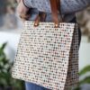Handmade square bag with base, button closure, leather handles and colorful small diamond pattern on beige background GR: Χειροποίητο τετράγωνο τσαντάκι με πάτο, κούμπωμα με κουμπί, δερμάτινα χερούλια και μοτίβο με μικρούς χρωματιστούς ρόμβους σε μπεζ φόντο