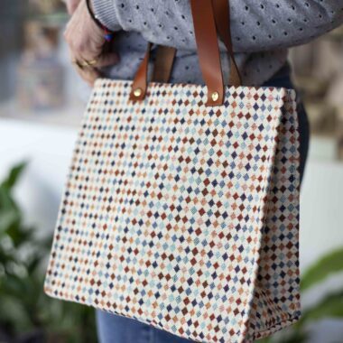 Handmade square bag with base, button closure, leather handles and colorful small diamond pattern on beige background GR: Χειροποίητο τετράγωνο τσαντάκι με πάτο, κούμπωμα με κουμπί, δερμάτινα χερούλια και μοτίβο με μικρούς χρωματιστούς ρόμβους σε μπεζ φόντο