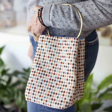 Handmade bag with large metal ring handle, button closure and colorful small diamond pattern on beige background GR: Χειροποίητο τσαντάκι με μεγάλο μεταλλικό κρίκο για χερούλι, κούμπωμα με κουμπί και μοτίβο με μικρούς χρωματιστούς ρόμβους σε μπεζ φόντο