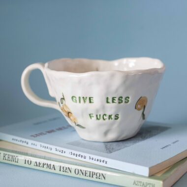 Χειροποίητη κεραμική κούπα με stamped μήνυμα “give less fucks” και πορτοκάλια σε cheerful citrus αισθητική. Handmade ceramic mug with stamped “give less fucks” text and orange illustrations in a cheerful citrus-inspired style.